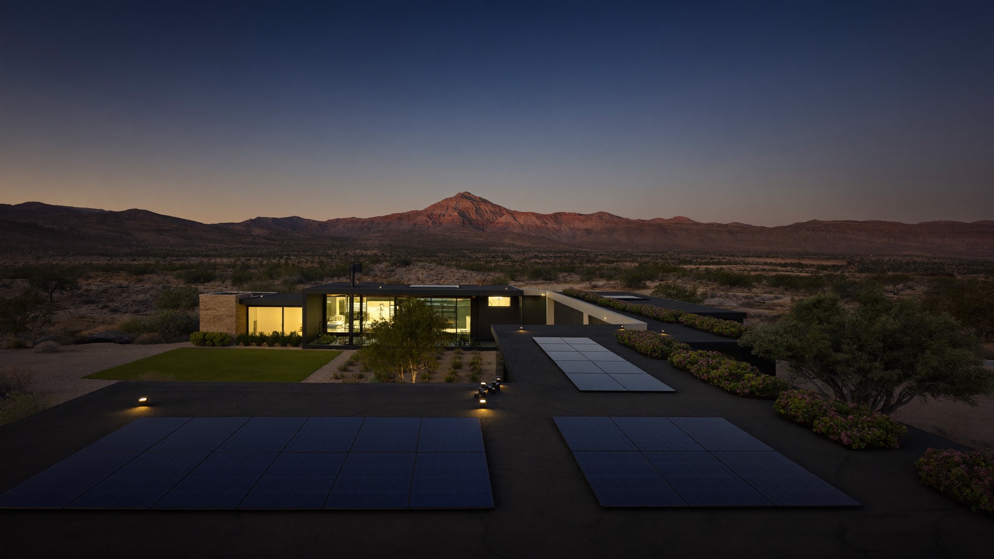 A desert-modern Paradise Valley home with a flush black rooftop solar array at dusk, Camelback Mountain behind